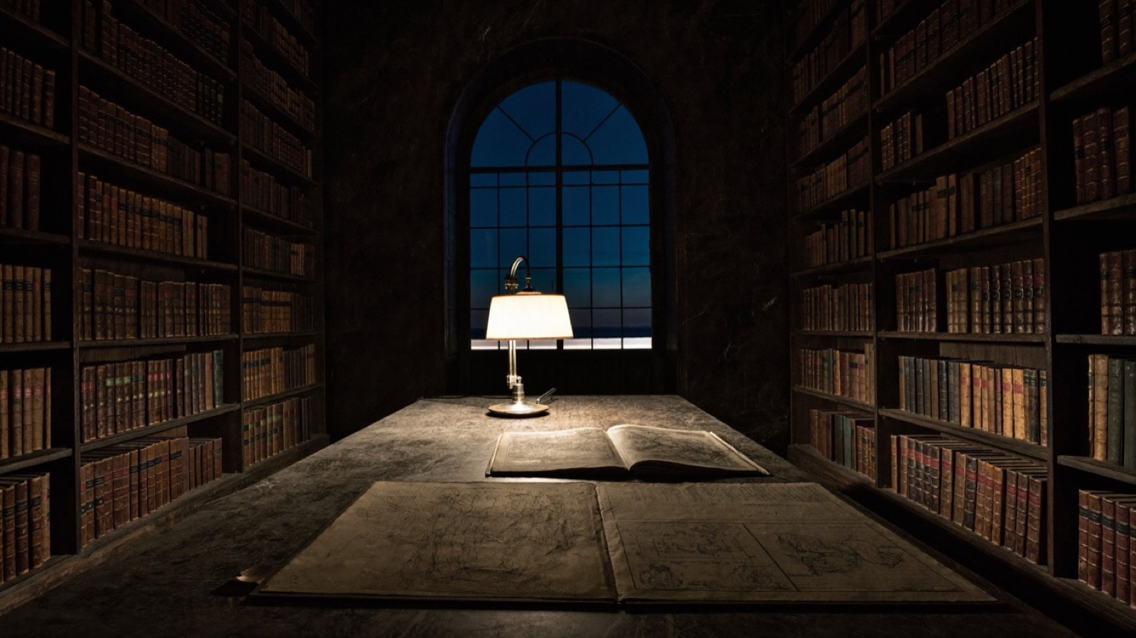 A library table spread with old maps and charts by lamplight